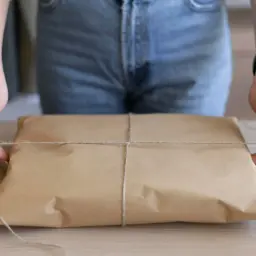 Dłonie zawiązują sznurkiem paczkę z brązowego papieru. Czy InPost dostarcza w soboty?